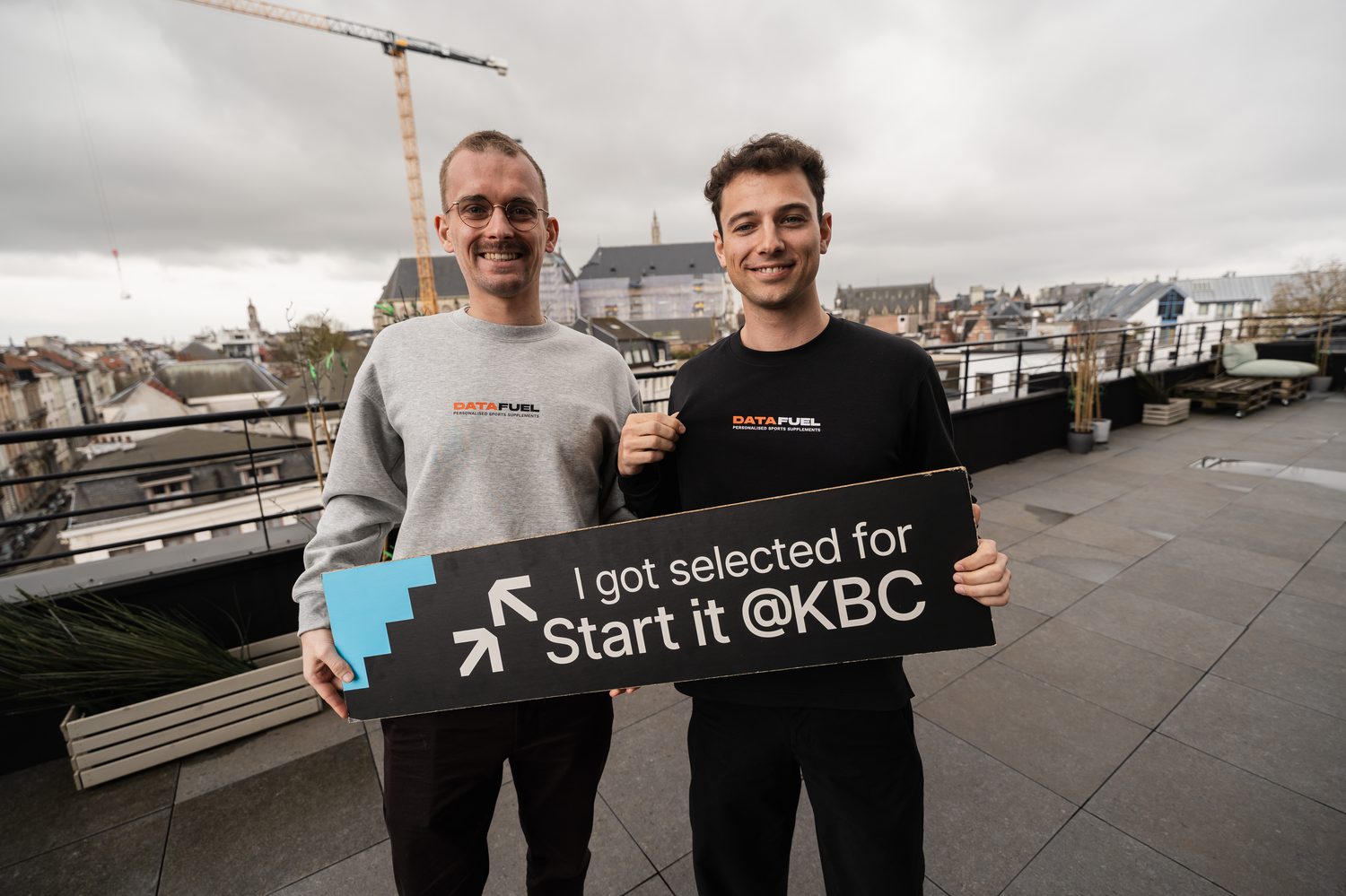 Numa and Simon on a rooftop, holding a sign reading "I got selected for Start it @KBC".